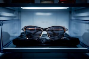 Illustration von einer hochwertigen Sonnenbrille, die in einem geöffneten Kühlschrank auf einem weichen Tuch im Gemüsefach liegt.