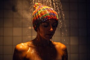 Illustration von einer Person, die unter der Dusche stehend eine bunte Wollmütze trägt, während Wasser über die Schultern rinnt.